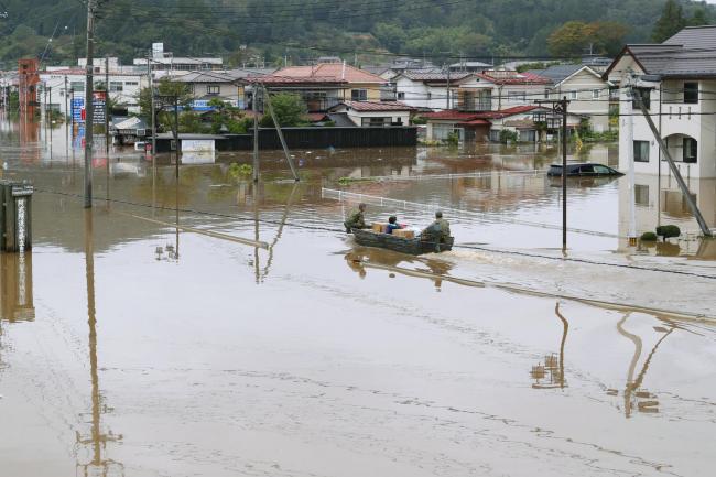 Rescuers carry supplies through a flooded street in Marumori town, Miyagi prefecture, Japan