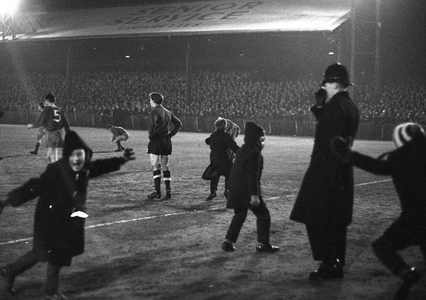 News and Star: Young fans pour onto the pitch after United's own-goal equaliser, as a policeman looks on