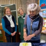 Volunteers, Cags Cousins cuts the cake, watched by volunteer, Mary Egerton and Charity President, Lady Elizabeth Leeming