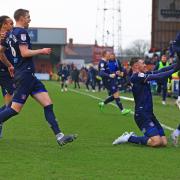 Ryan Edmondson celebrates with a knee slide in front of the travelling fans as team-mates and coaches race to join in